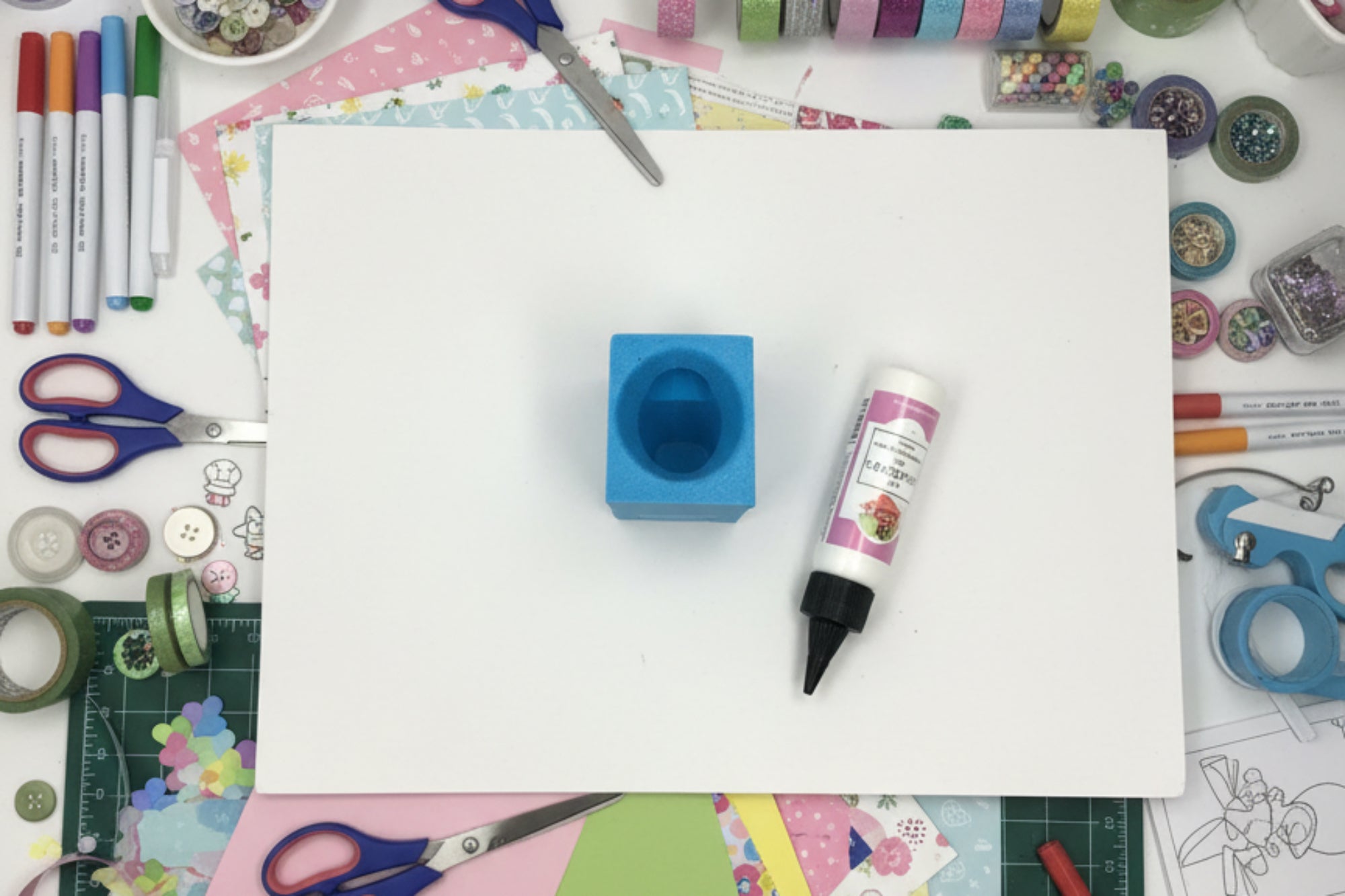 Blue foam block with a cylindrical indentation on a white surface, with a bottle of glue in the background.