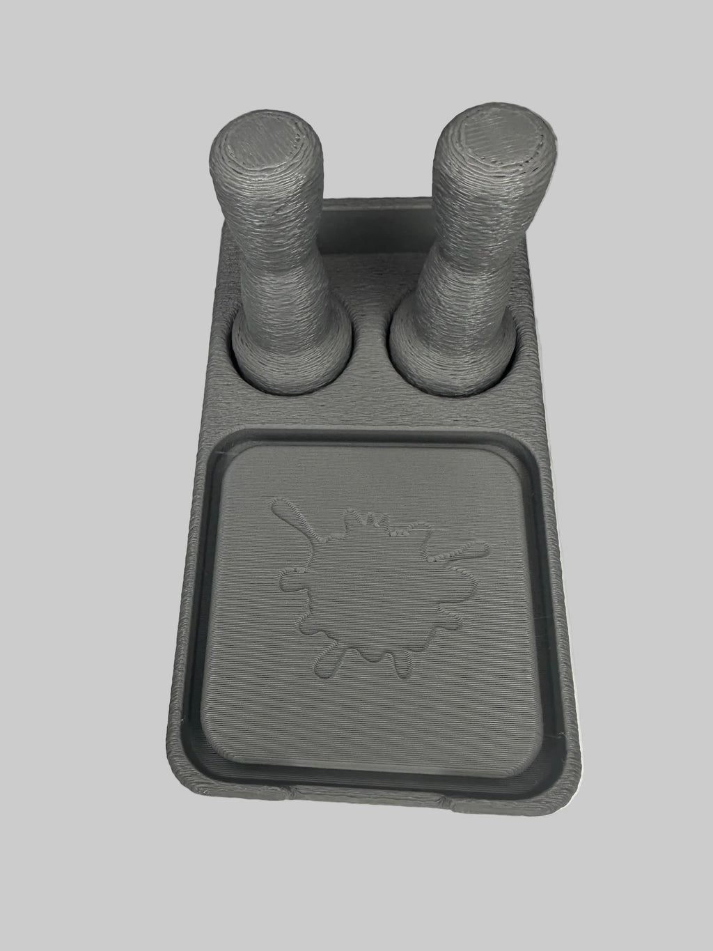 Gray plastic component with two cylindrical protrusions on a white surface