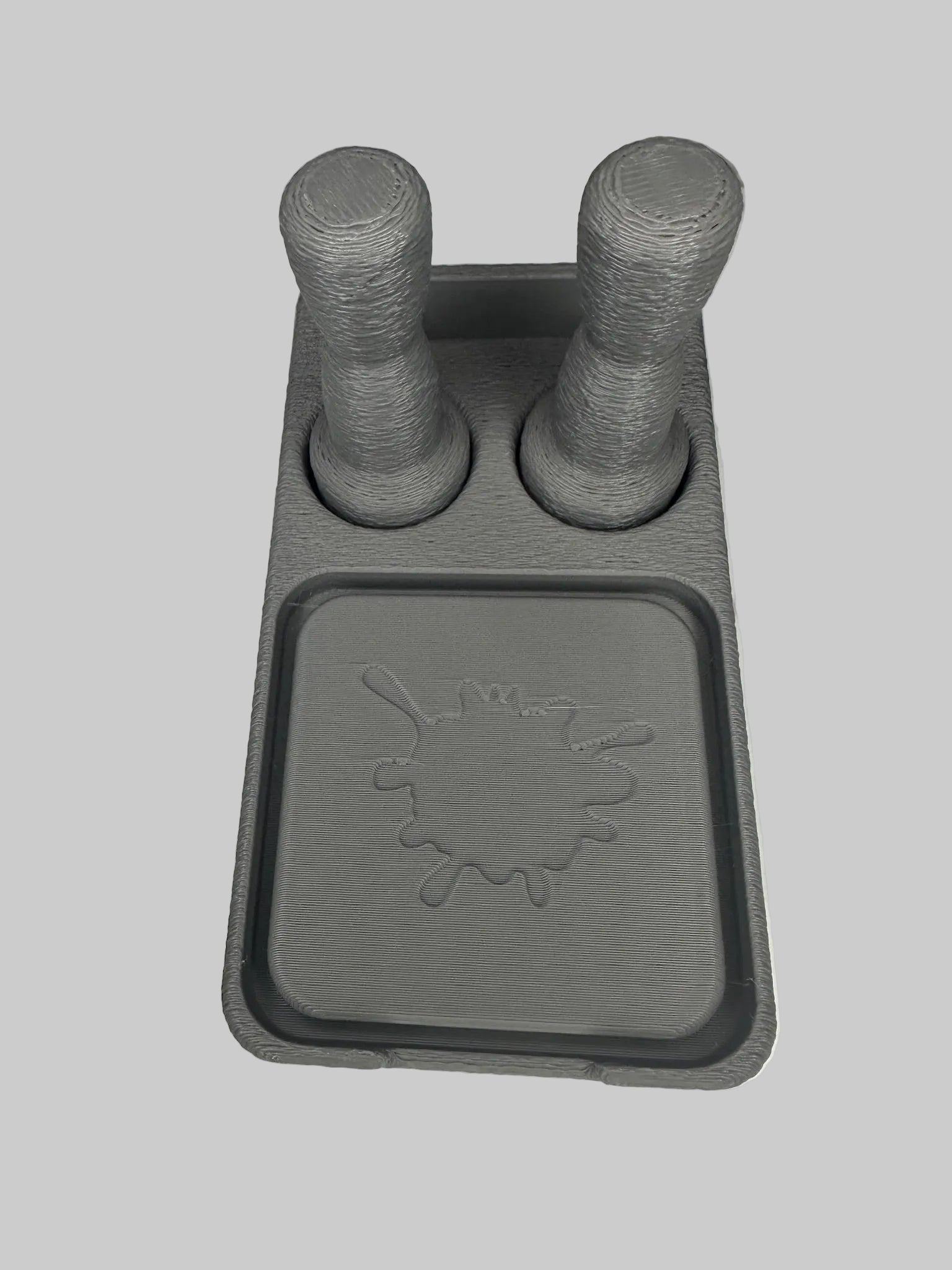 Gray plastic component with two cylindrical protrusions on a white surface